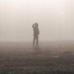 Silhouette of a person walking along a foggy field, hand scratching his/her head