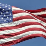 Closeup of the United States of America flag waving in the breeze, stars on the left side, on a sky blue background.