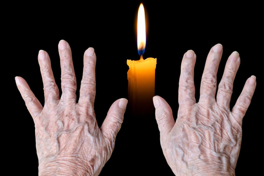 Elderly hands warming themselves over a candle